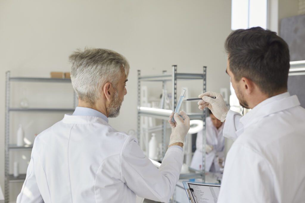 Professional medical scientists working in the laboratory of modern medicine. Two unrecognizable male scientists, standing with their backs to the camera, look at a test tube with liquid.
